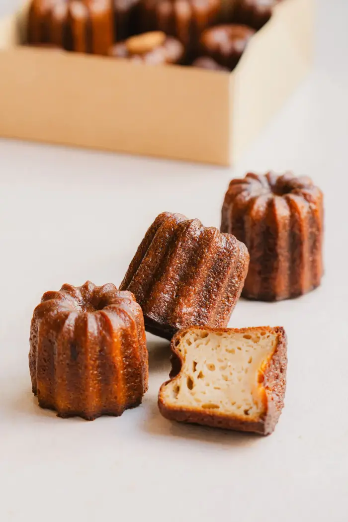 Boîte de cannelés artisanaux à emporter, dont un croqué qui dévoile son cœur moelleux, chez Coco Cannelés à Paris