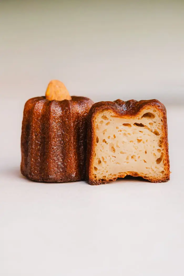 Cannelé artisanal coupé en deux révélant sa mie moelleuse et alvéolée sous une croûte caramélisée