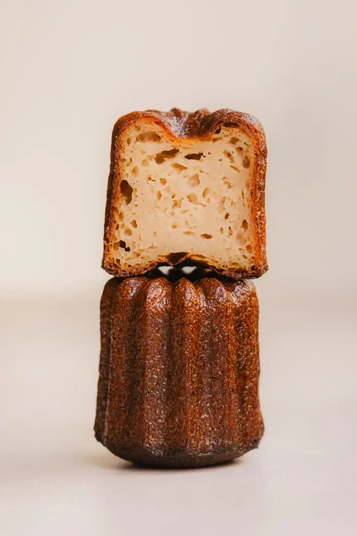 Cannelé caramélisé surmonté de sa tranche coupée, mettant en valeur la mie moelleuse et humide typique du cannelé