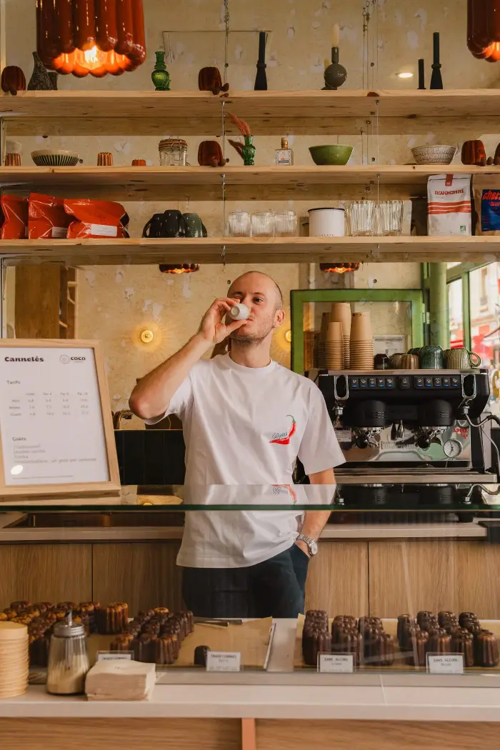 Le fondateur de Coco Cannelés dégustant un café de spécialité derrière le comptoir de la boutique de cannelés artisanaux à Paris 11e