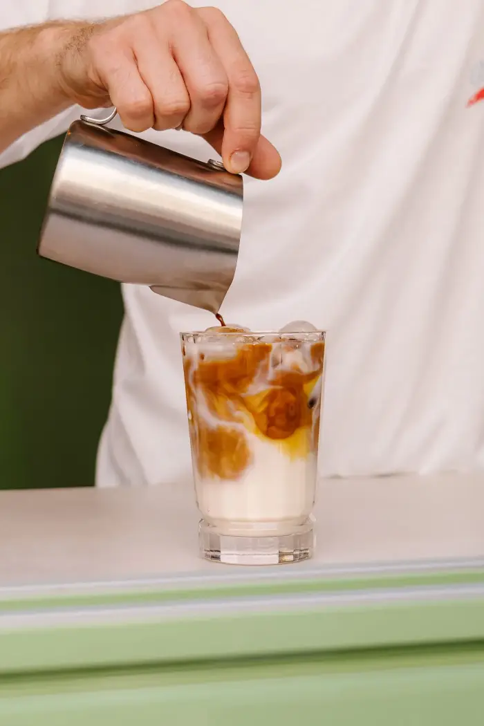 Préparation d'un latte glacé au café de spécialité, café versé sur le lait et les glaçons chez Coco Cannelés