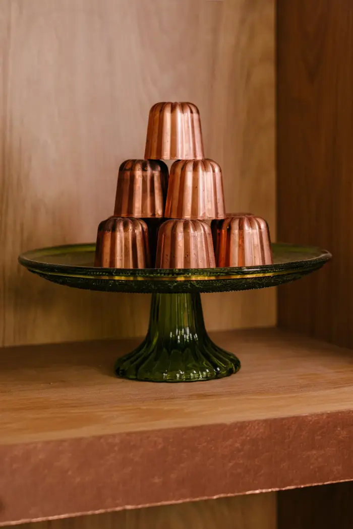 Pyramide de moules à cannelés en cuivre traditionnels posée sur un présentoir en verre vert dans la boutique Coco Cannelés