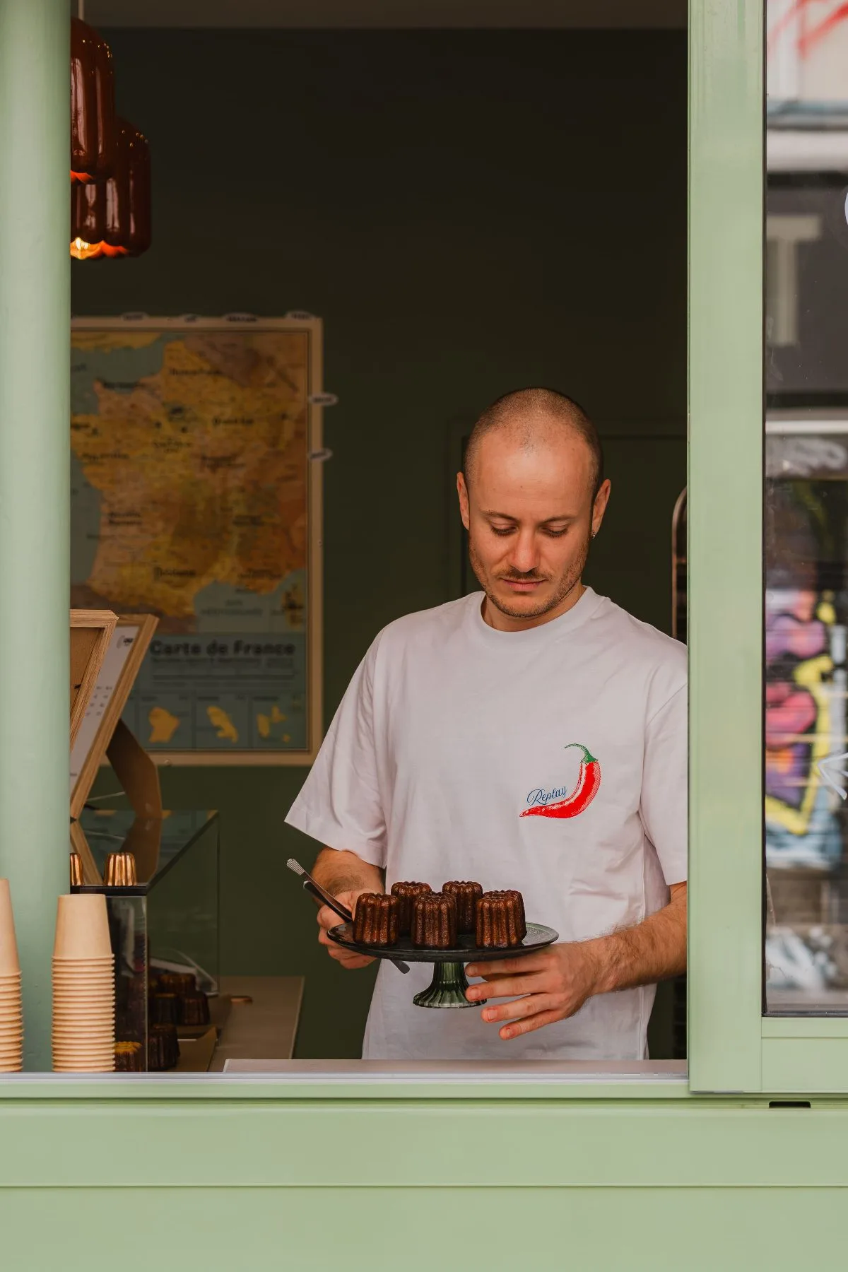 Coco à la fenêtre de la boutique avec un présentoir de cannelés